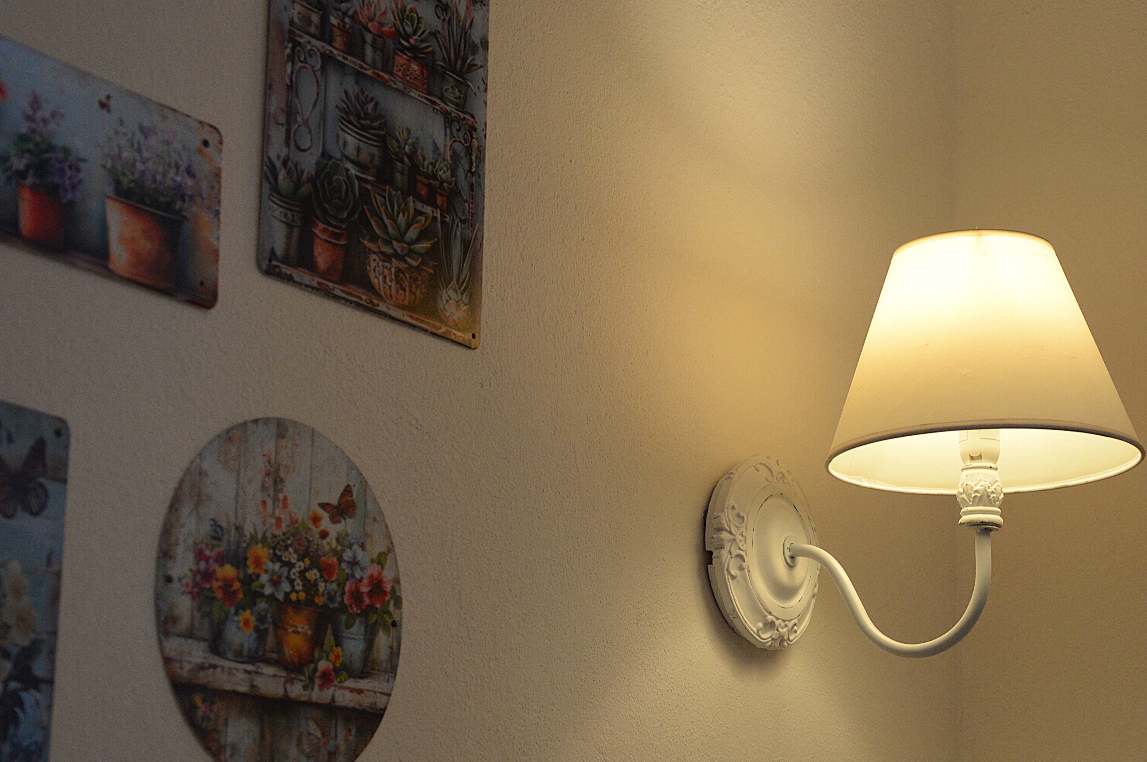 A wall-mounted lamp with a white shade, surrounded by various decorative wall art featuring plants and flowers.