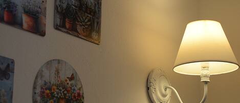 A wall-mounted lamp with a white shade, surrounded by various decorative wall art featuring plants and flowers.