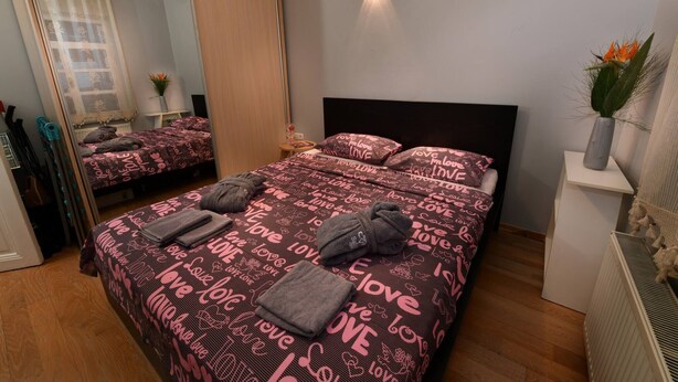Un dormitorio con cama, espejo, mesita de noche y lámpara de pared.