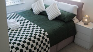 A neatly made bed with a checkered blanket, two pillows, and a bedside lamp. - Modern 3-Bed House Leeds | Sleeps 7 | Free Parking | Contractor Friendly | Wi-Fi (Leeds)
