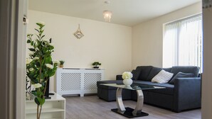 A modern living room with a grey sofa, a glass coffee table, a potted plant, and a white cabinet. - Modern 3-Bed House Leeds | Sleeps 7 | Free Parking | Contractor Friendly | Wi-Fi (Leeds)
