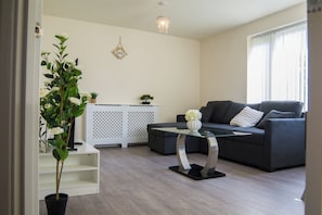 Ein modernes Wohnzimmer mit einem grauen Sofa, einem Glastisch, einer Topfpflanze und einem weißen Schrank.