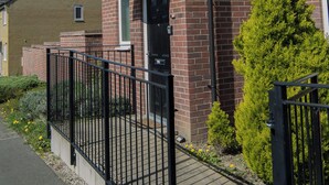 A red brick residential building with a black door, a small window, and a black metal fence. - Modern 3-Bed House Leeds | Sleeps 7 | Free Parking | Contractor Friendly | Wi-Fi (Leeds)