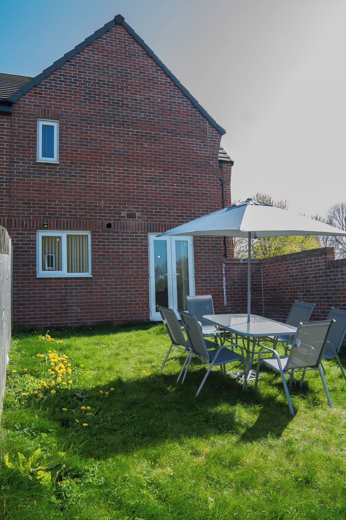 A brick building with a patio table and chairs, a white umbrella, and a small window.