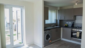A modern kitchen with a washing machine, oven, and a sliding glass door leading to a balcony. - Modern 3-Bed House Leeds | Sleeps 7 | Free Parking | Contractor Friendly | Wi-Fi (Leeds)