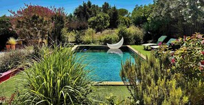 A swimming pool with a crescent moon sculpture, surrounded by lush greenery and a wooden deck. - Villa with private pool between Nîmes and Uzès (Saint-Mamert-du-Gard)