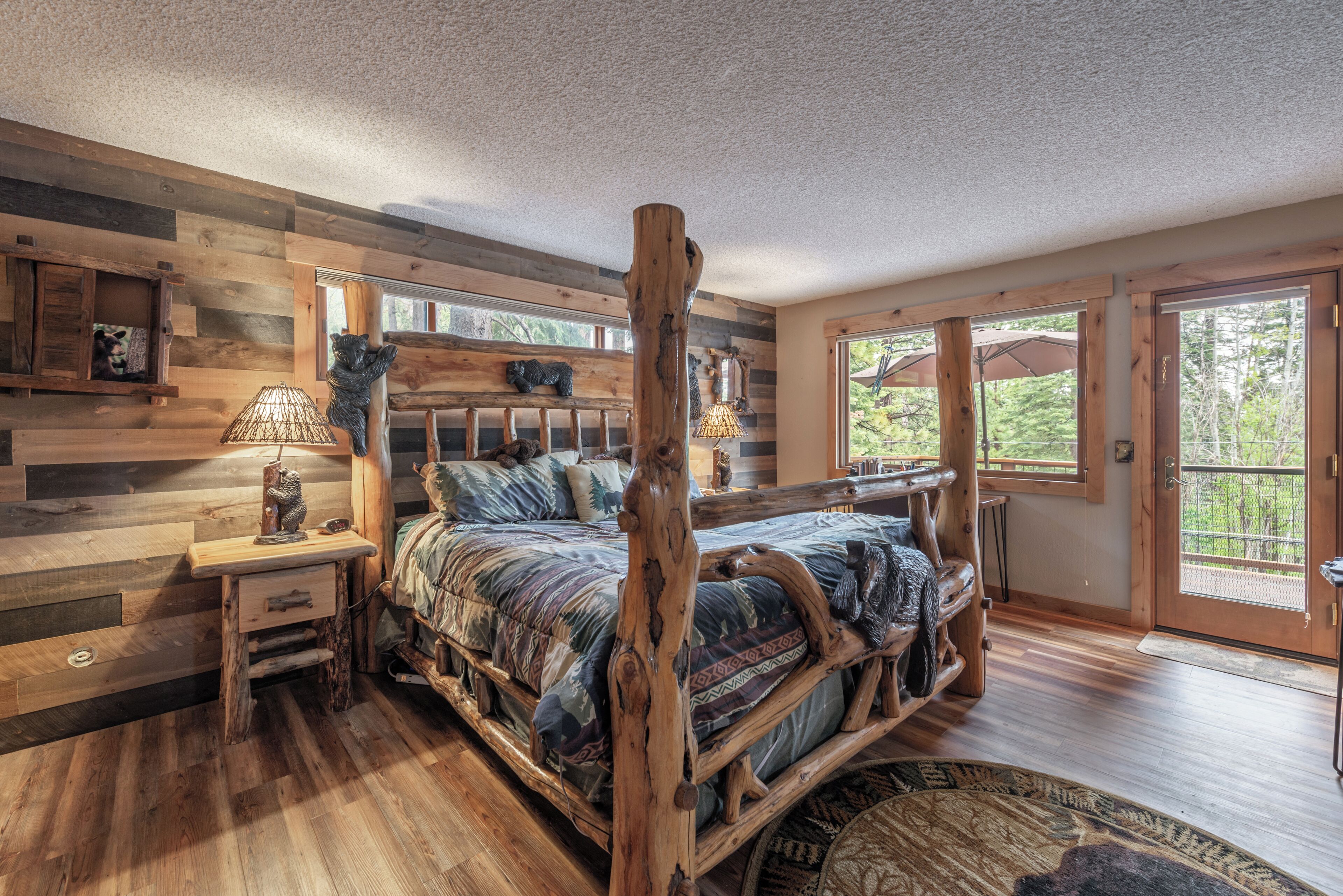 A rustic wooden bedroom with a four-poster bed, a nightstand, and a window with a view of greenery.