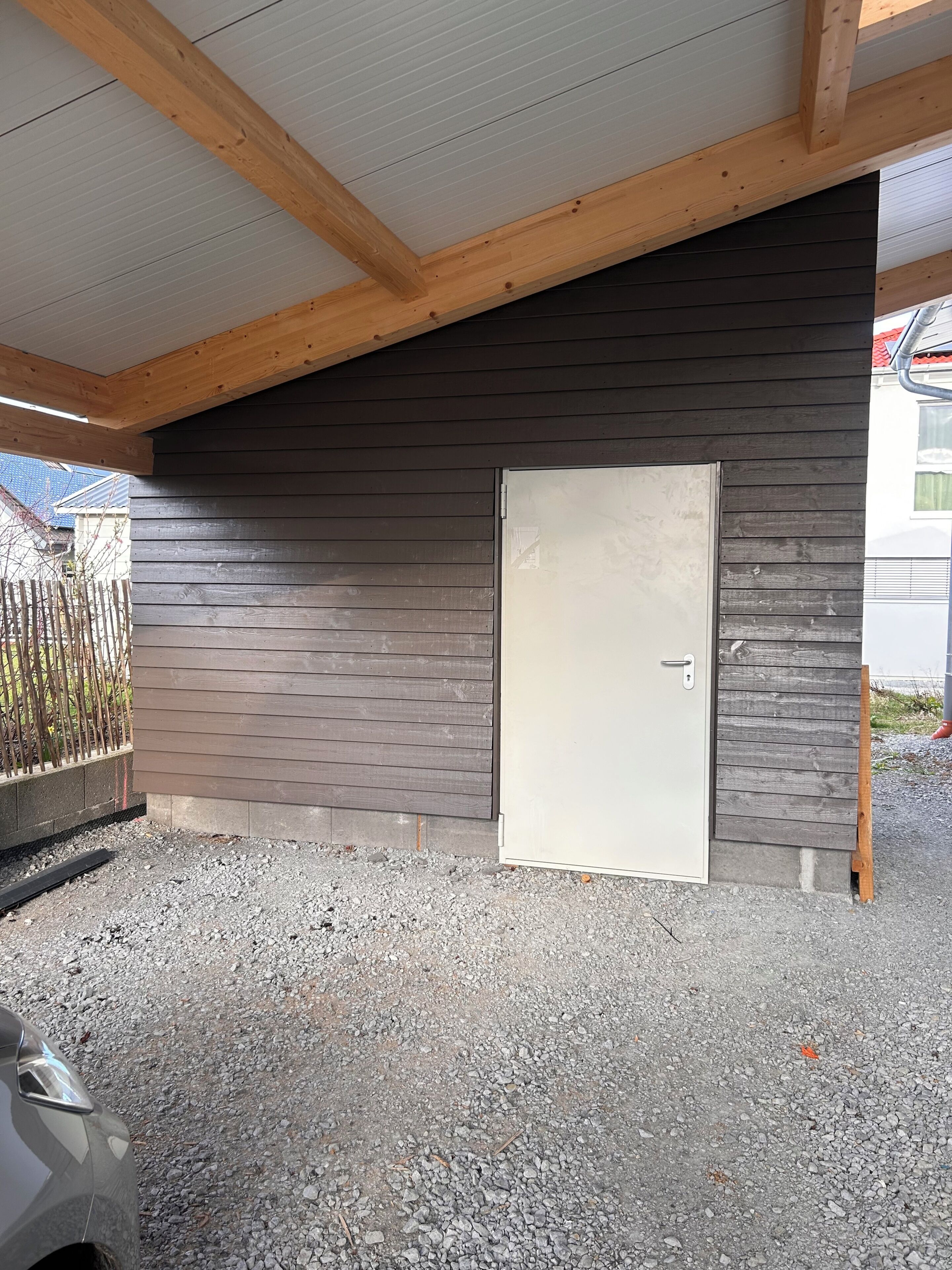 Et overdækket udendørs område med træloft, en dør og grusgrund.