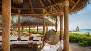 A beach cabana with wooden furniture, a hanging chair, and a view of the ocean. - Grand Mayan Vidanta 2BR Luxury Suite + Pools & Beach (Playa Paraiso)