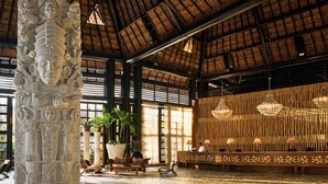 A spacious lobby with a high ceiling, a large stone sculpture, potted plants, a reception desk, and modern chandeliers. - Grand Mayan Vidanta 2BR Luxury Suite + Pools & Beach (Playa Paraiso)