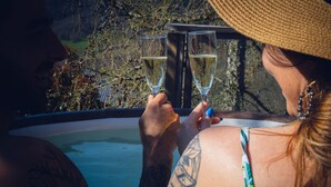 Two people toasting with champagne glasses in a hot tub with a view of trees and a wooden structure. - Small cottage in the heart of Beaujolais (Rivolet)