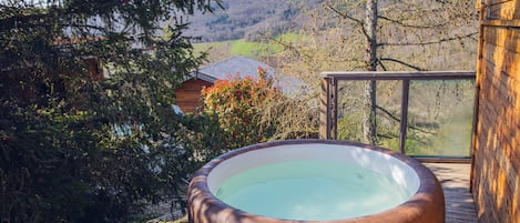 Ein Whirlpool auf einer Holzterrasse mit Blick auf ein Haus und Bäume.