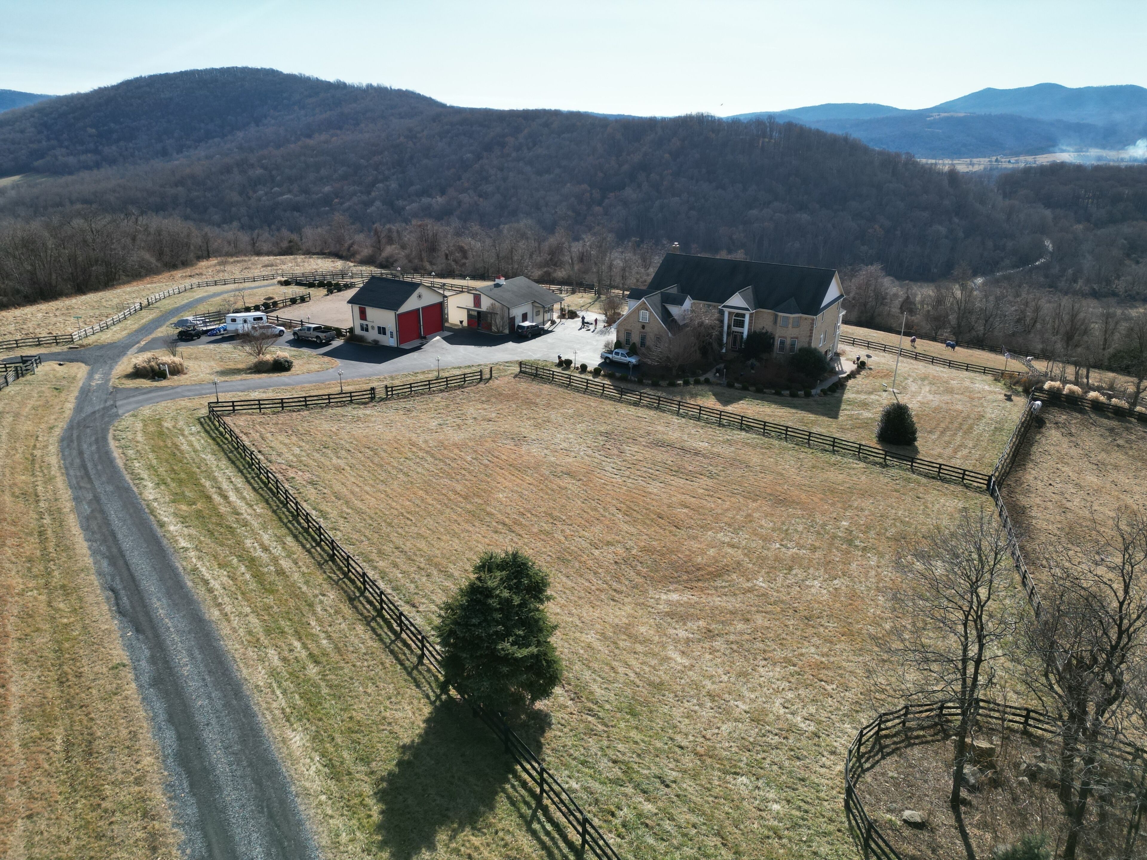 An aerial view of a rural property with a large barn, a farmhouse, and fenced fields.