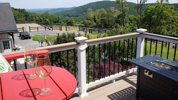 A balcony with a table, two wine glasses, and a view of a fenced area with a truck and a building in the background. - "The Love Nest" - Stunning Views overlooking the Shenandoah in Wine Country (Markham)