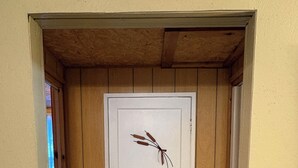 En vit dörr med en dekorativ växt på dörrskylten, placerad i en hall med träväggar och ett betonggolv.