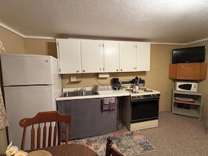 A compact kitchen with white cabinets, a stove, a microwave, and a refrigerator.