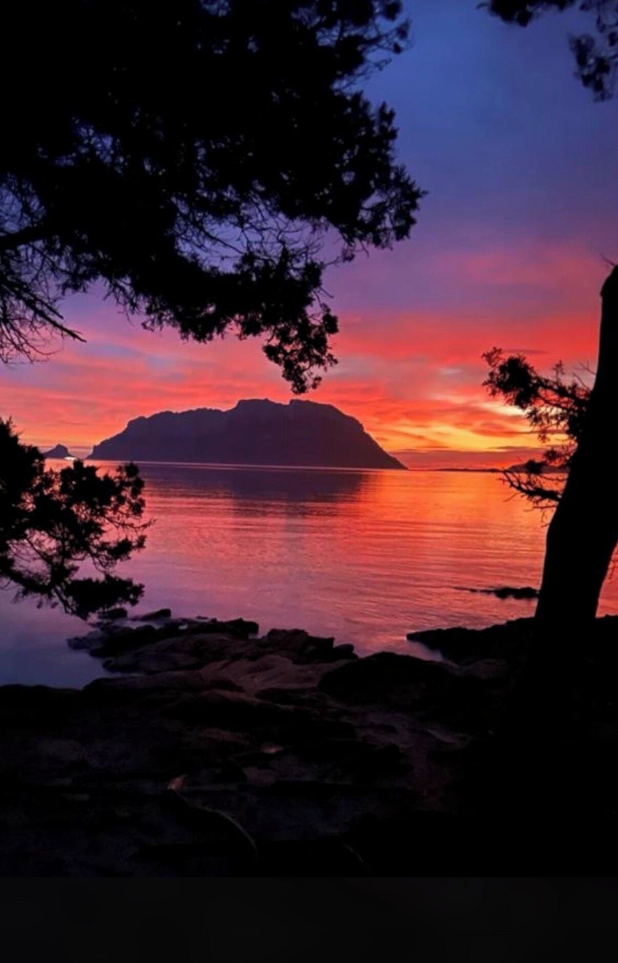 Un coucher de soleil paisible sur une étendue d’eau, avec la silhouette d’une île lointaine à l’horizon.