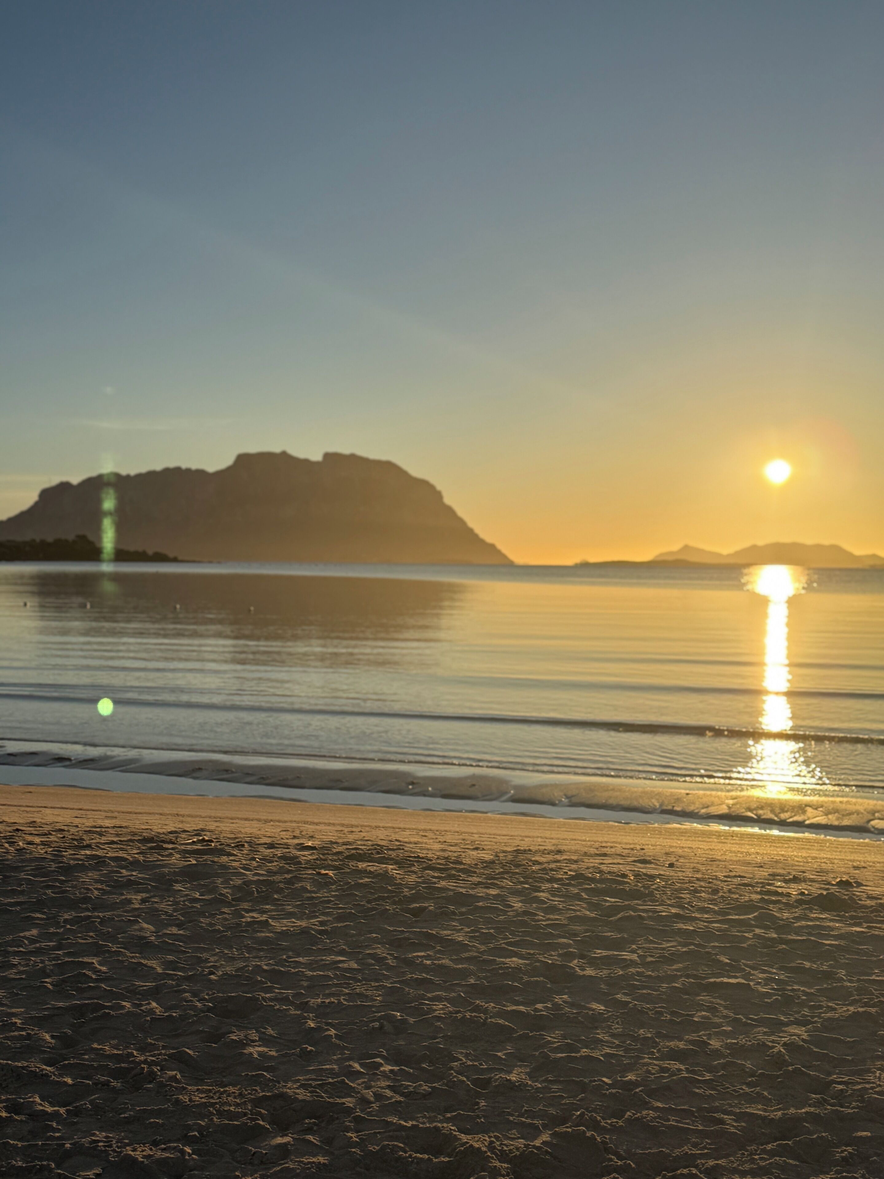 Ein Strand mit ruhigem Wasser, wolkenlosem Himmel und Bergen im Hintergrund.