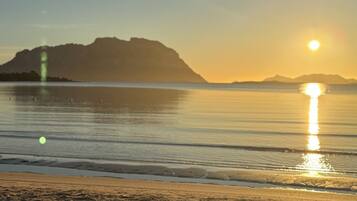 Ein Strand mit ruhigem Wasser, wolkenlosem Himmel und Bergen im Hintergrund.