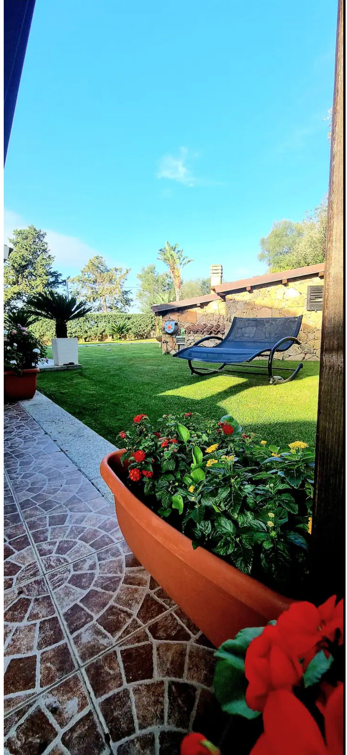 A patio with a tiled floor, a stone wall, and a blue lounge chair.