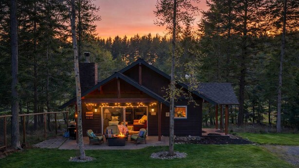 A cabin with a covered patio, outdoor seating, and a view of the forest. - Chickadee Cabin - Boutique Stay close to Downtown (Whitefish)