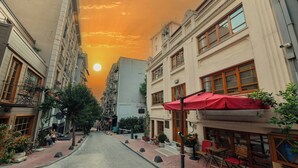 Een smalle stadstraat met gebouwen aan beide zijden, een rode paraplu en terrasplekken.