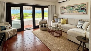Ein Wohnzimmer mit Deckenventilator, einer Sofagarnitur, einem Couchtisch und Blick durch Glastüren.