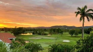 Ein Golfplatz mit einem Haus im Vordergrund und einem Sonnenuntergang im Hintergrund.