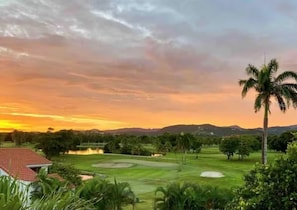 Ein Golfplatz mit einem Haus im Vordergrund und einem Sonnenuntergang im Hintergrund.