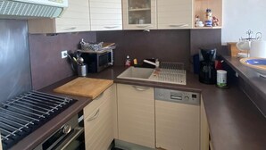 A compact kitchen with a gas stove, oven, dishwasher, and a checkered floor. - Duplex T2 first line on the beach with parking Palavas/Carnon (Palavas-les-Flots)