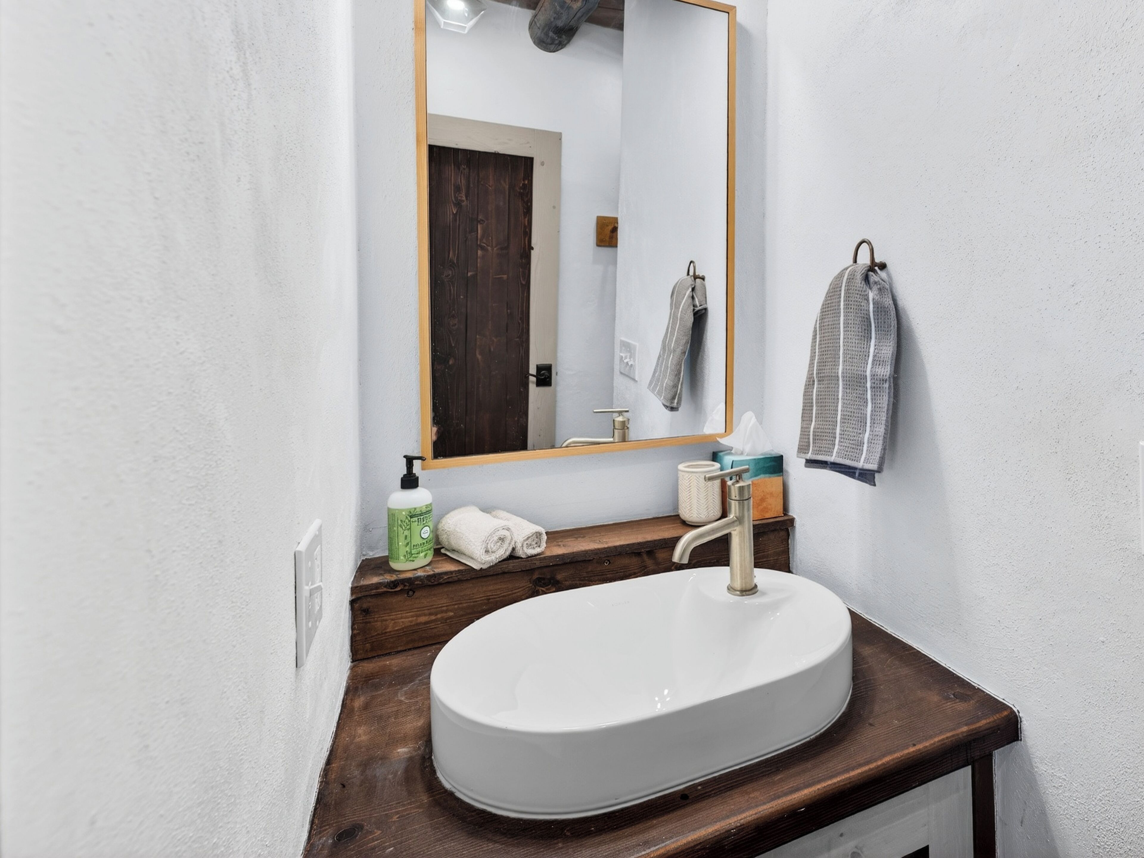 A bathroom with a white sink, wooden vanity, a mirror with a wooden frame, and towels.