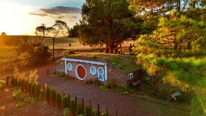 Un edificio rústico de piedra con ventanas circulares, rodeado por un paisaje rural con árboles y un campo.