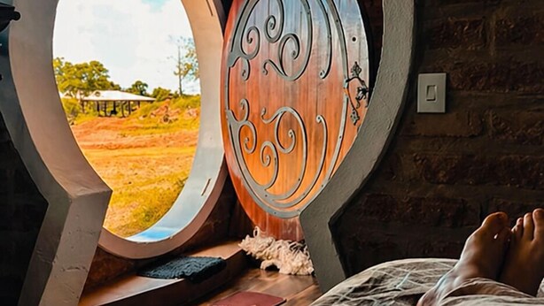 A bedroom with a circular window, a bed, and a rustic brick wall. - Cypress County - Hobbit Themed Lodging (Condor)
