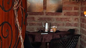 Un comedor con pared de ladrillo, dos cuadros, una cafetera, tazas y sillas.