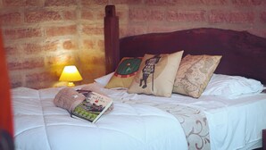 A bed with a book, pillows, and a lamp in a room with brick walls. - Cypress County - Hobbit Themed Lodging (Condor)