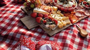 Een picknickopstelling met een geruit tafelkleed, diverse kazen, fruit en een rode roos.
