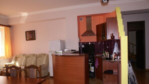 A living room with a sofa, a wooden coffee table, a kitchen area with a stove, and a refrigerator. - Karin's B&B (Sisian)