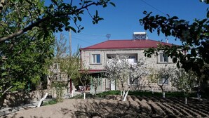 A stone building with a red roof, surrounded by trees and a garden. - Karin's B&B (Sisian)
