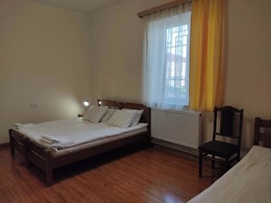 A bedroom with a wooden bed, a chair, a radiator, and a window with curtains.