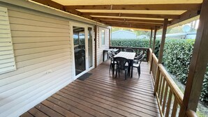 Une terrasse en bois avec une table et des chaises, un espace couvert avec une rambarde, et une porte-fenêtre coulissante donnant sur un garage.