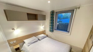 Une chambre à coucher comprenant un lit, une table de chevet, une étagère intégrée, une fenêtre avec des rideaux et un luminaire fixé au mur.