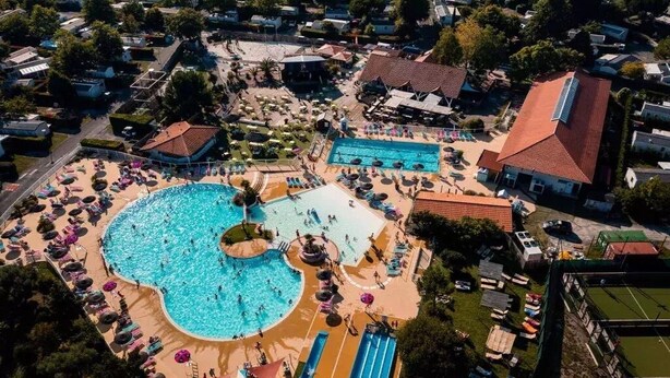 Vue aérienne d’un complexe hôtelier doté d’une grande piscine centrale, de plusieurs piscines plus petites et de divers espaces de détente en plein air.