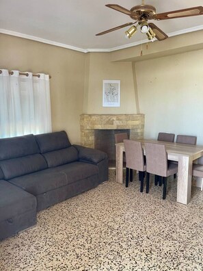 A living room with a sofa, a dining table with chairs, a fireplace, and a ceiling fan.