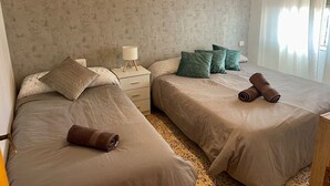 Ein Doppelzimmer mit zwei Betten, einem Nachttisch, einer Lampe und einem Fenster mit Vorhängen.