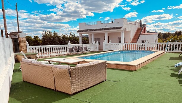 Ein Poolbereich auf dem Dach mit weißem Zaun, einer Korbsessel-Lounge und einem zweistöckigen Gebäude im Hintergrund.