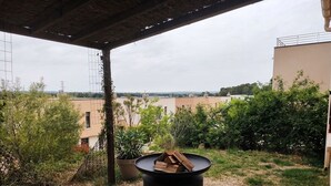 An outdoor patio area with a fire pit, gravel ground, and a view of buildings and greenery. - Family home with garden, trampoline and ideal location (Piolenc)