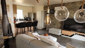 A modern living room with a sofa, a TV, and hanging light fixtures. - Family home with garden, trampoline and ideal location (Piolenc)