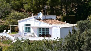 Um edifício branco com antena parabólica, piscina e um pátio com cadeiras.