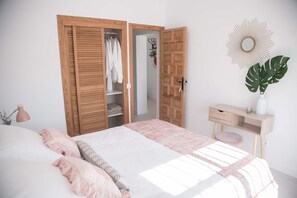 Ein Schlafzimmer mit Bett, Kleiderschrank, Schreibtisch mit Pflanze und einem Wandspiegel.