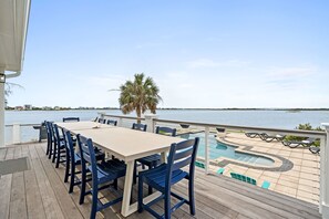 Une terrasse avec une table et des chaises, une piscine avec des chaises longues et une vue sur l’eau.
